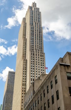 Rockefeller Center Skyscraper, view from the side, low angle during winter day with cloud sky, American flag in front of the Building, vertical