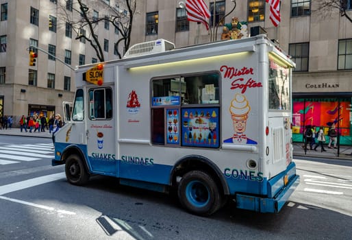 Mister Softee Ice Cream Truck waiting at red traffic light in front of crosswalk at Fifth Avenue, view from the side, New York City during winter day, horizontal