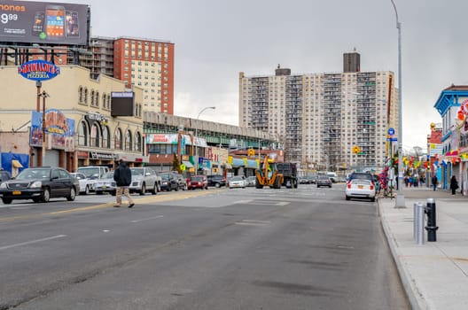 City Street with different shops, stores and restaurants at Coney island, Brooklyn with lots of Traffic and People walking on the sideway, Residential Buildings in the background, New York City during winter day with cloudy sky, horizontal