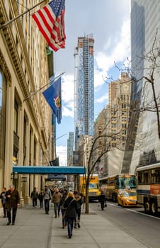 Smythson and Metropolitan with Park Hyatt Skyscraper Construction Site at W57th ST, People walking on sidewalk, Busses and taxi passing by on the city street, New York City during sunny winter day with cloudy sky, vertical