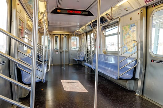 Subway New York City indoors, empty, destination to Coney island, Brooklyn, red lettering on screen at the roof of the train, indoors with blue benches, driving above ground during sunny day, horizontal