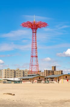 Red Parachute Jump at Luna Park Amusement Park, Coney island, Brooklyn with empty Beach and Buildings in front during sunny winter day with cloudy sky, New York City, vertical