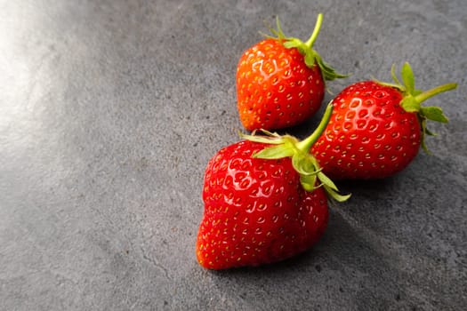 Three  red ripe strawberries over dark background with copy space