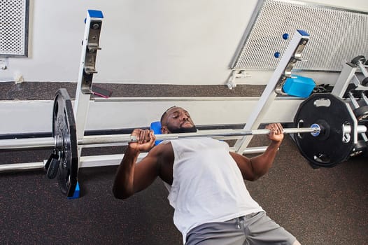 An African American man does a bench press lying on a bench in the gym. High quality photo