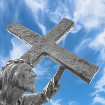 Statue of Jesus carrying his cross, on the way to his crucifixion. Ideal for the easter concept, resurrection and other. Blue sky with white clouds on background.