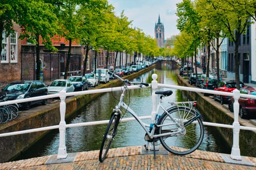 Picturesque Holland cityscape view - bicycle on bridge and canal with cars parked along and Oude Kerk old church in street of Delft, Netherlands