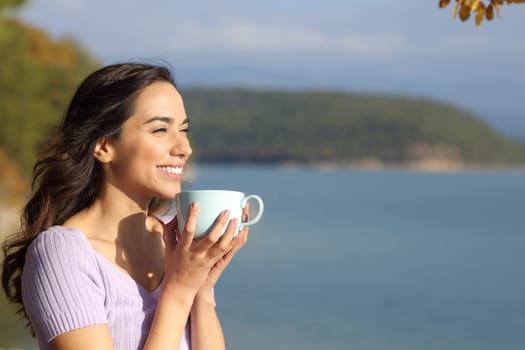 Happy woman drinking coffee looking away in nature