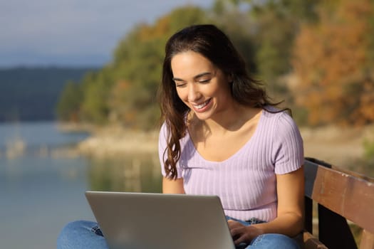 Happy woman using a laptop in a lake on holiday