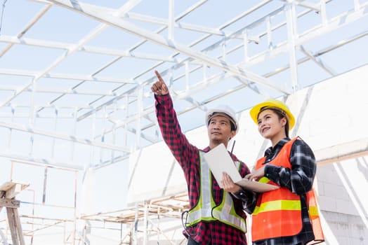 Asian engineer foreman worker man and woman working at building construction site use laptop and talking with radio, engineering hold computer and radio discuss and control worker employee to building