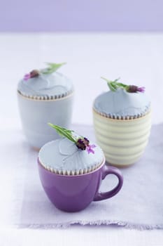 Three cupcakes with lavender buttercream and lavender flowers on a purple tablecloth