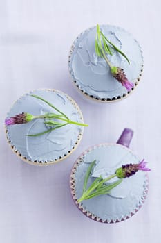 Three cupcakes with lavender buttercream and lavender flowers on a purple tablecloth