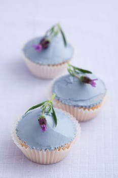 Three cupcakes with lavender buttercream and lavender flowers on a purple tablecloth
