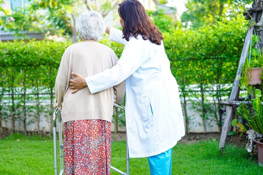 Doctor help Asian elderly woman disability patient walk with walker in park, medical concept.