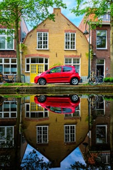 Red car on canal embankment in street of Delft with reflection and bicycle. Delft, Netherlands