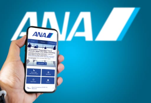 Tokyo, JAP, January 2022: Hand holding a phone with ANA All Nippon Airways flight booking application. Ana logo blurred on a blue background. Booking airline tickets