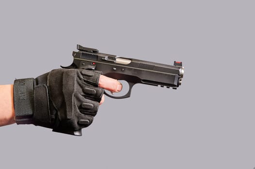 A man's hand holds a black pistol in his hand on a gray background. High quality photo