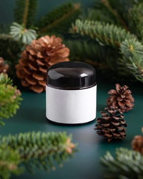 Brown glass jar near fir branches and pine cones on dark green close up. Brand packaging mockup. Skincare beauty product, cream or serum. Healthcare natural cosmetics concept