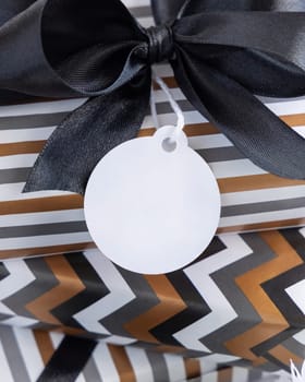 Present with round blank gift tag and black bow close up. Gift boxes wrapped in Striped and chevron geometric paper near black and white decor. Christmas, New Year, Birthday, Anniversary label mockup