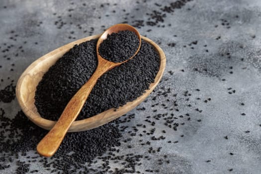 Indian spice Black cumin (nigella sativa or kalonji) seeds in bowl with spoon on grey table close up with copy space. Traditional medicine, healthy and vegetarian food concept.