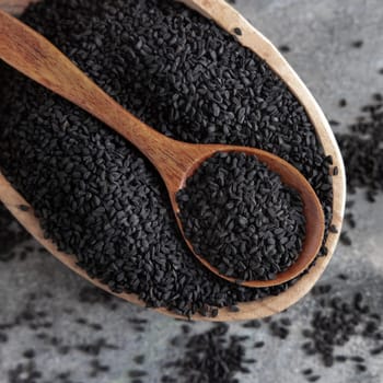 Indian spice Black cumin (nigella sativa or kalonji) seeds in bowl with spoon on grey table top view. Traditional medicine, healthy and vegetarian food concept.