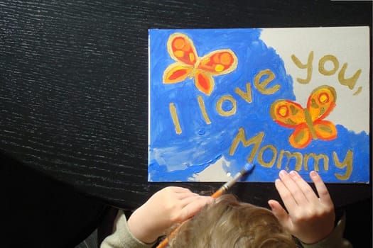 hand of a little child painting a picture with butterflies for mommy at mother's day with the text I love you mommy