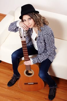 Young woman with a guitar sitting on a sofa