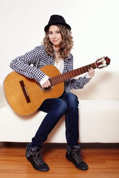 Young woman playing the guitar and sitting on a sofa