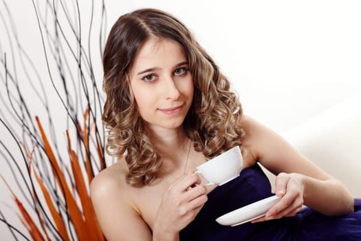 Young woman wearing an evening dress and having a cup of coffee