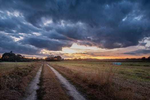 Dirt road through the field and clouds after sunset, summer view