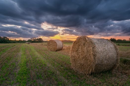 Straw bales in the field and clouds after sunset, summer view
