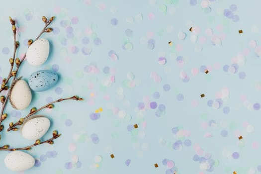 Happy Easter holiday, spring concept. Flat lay with tree branches, flower twigs with white, colorful quail eggs. Blue table background, copy space. Easter home decoration, greeting card, invitation