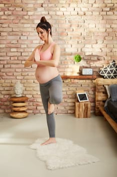 Pregnant woman doing yoga exercise at home standing.