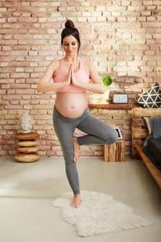 Pregnant woman doing yoga exercise at home standing.