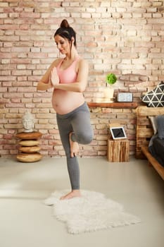 Pregnant woman doing yoga exercise at home standing.