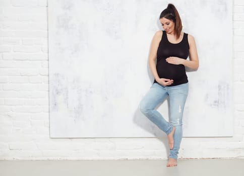 Fashion portrait of happy pregnant woman in jeans.. against white wall with copyspace.