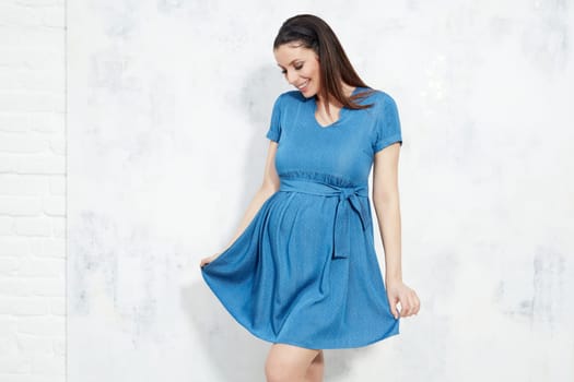 Fashion portrait of happy pregnant woman in blue summer dress against white wall with copyspace.