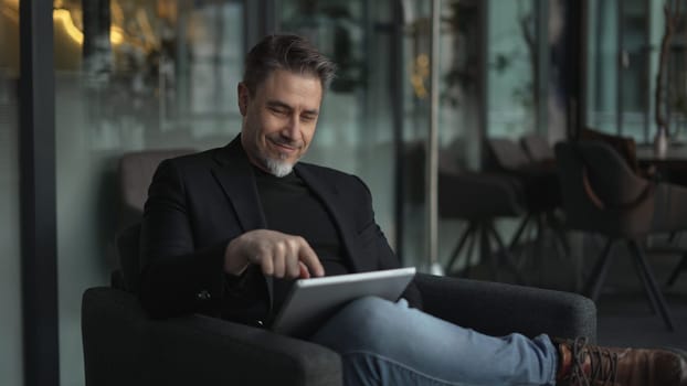 Businessman using tablet computer in office. Happy middle aged man in business casual, Entrepreneur working online, reading finance report, thinking.
