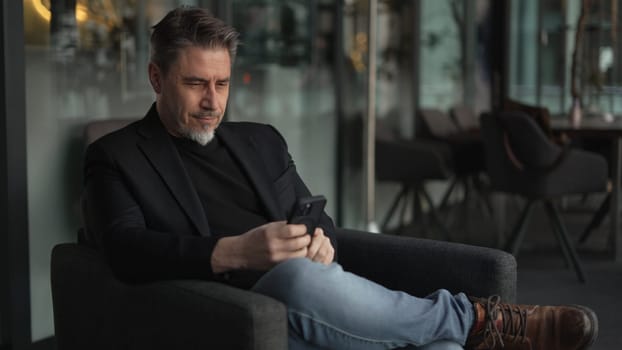 Businessman using phone in office. Serious middle aged man in business casual, Entrepreneur working online, reading finance report, thinking. .