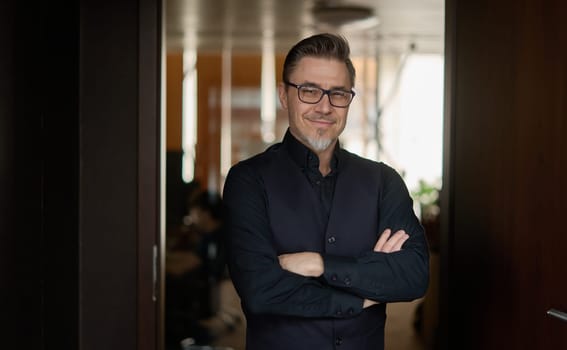 Business portrait - businessman standing in office, smiling. Happy middle aged, mid adult man in black jacket.