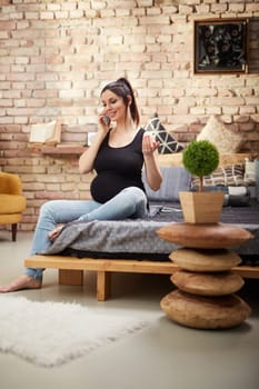Happy pregnant woman sitting at home smiling, relaxing talking on phone.
