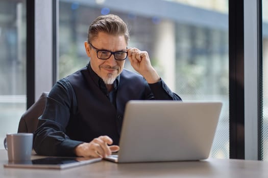 Businessman using laptop computer in office. Happy middle aged man, entrepreneur, small business owner working online.