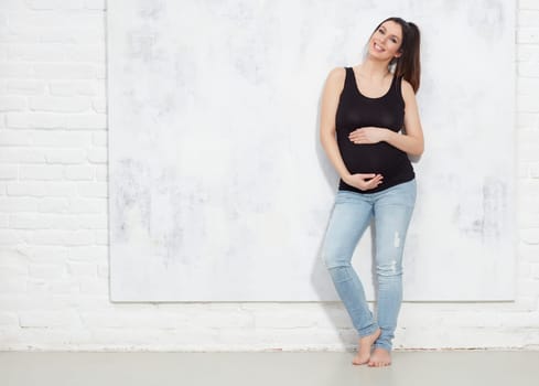Fashion portrait of happy pregnant woman in jeans.. against white wall with copyspace.