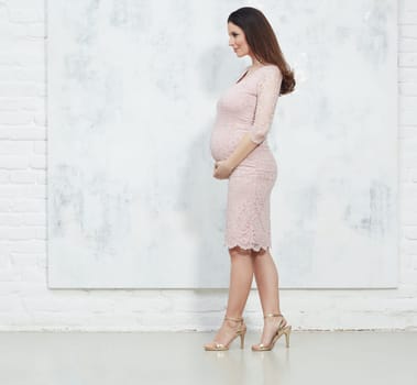 Fashion portrait of happy pregnant woman in elegant dress against white wall with copyspace.