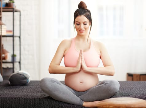 Pregnant woman doing yoga exercise at home relaxing with meditation.