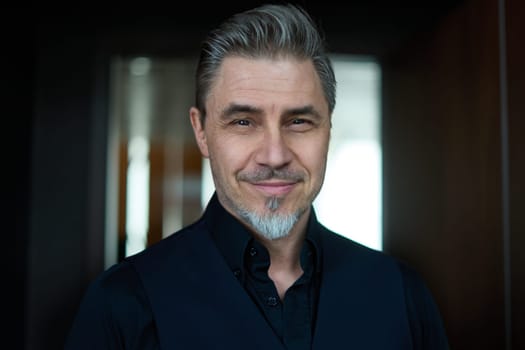 Business portrait - businessman standing in office, smiling. Happy middle aged, mid adult man in black jacket.