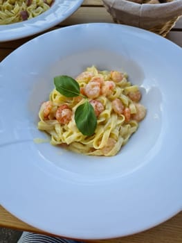 Plate of delicious pasta with shrimps on white wooden table, top view