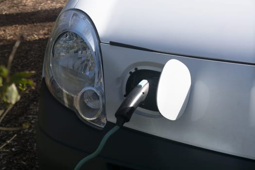 EV car or electric vehicle at the charging station with the power cord adapter plugged into blurred nature with blue energy power effect. Environmentally friendly sustainable energy concept. .