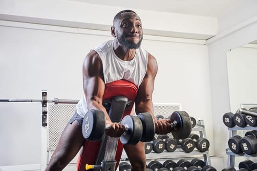 An African-American man shakes his biceps on an inclined bench in the gym. High quality photo