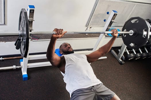 An African American man does a bench press lying on a bench in the gym. High quality photo