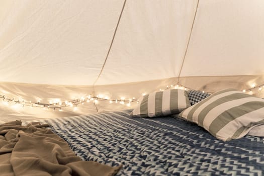 side view closeup of empty glamping house tent interior detail with bed pillows and intimate lights